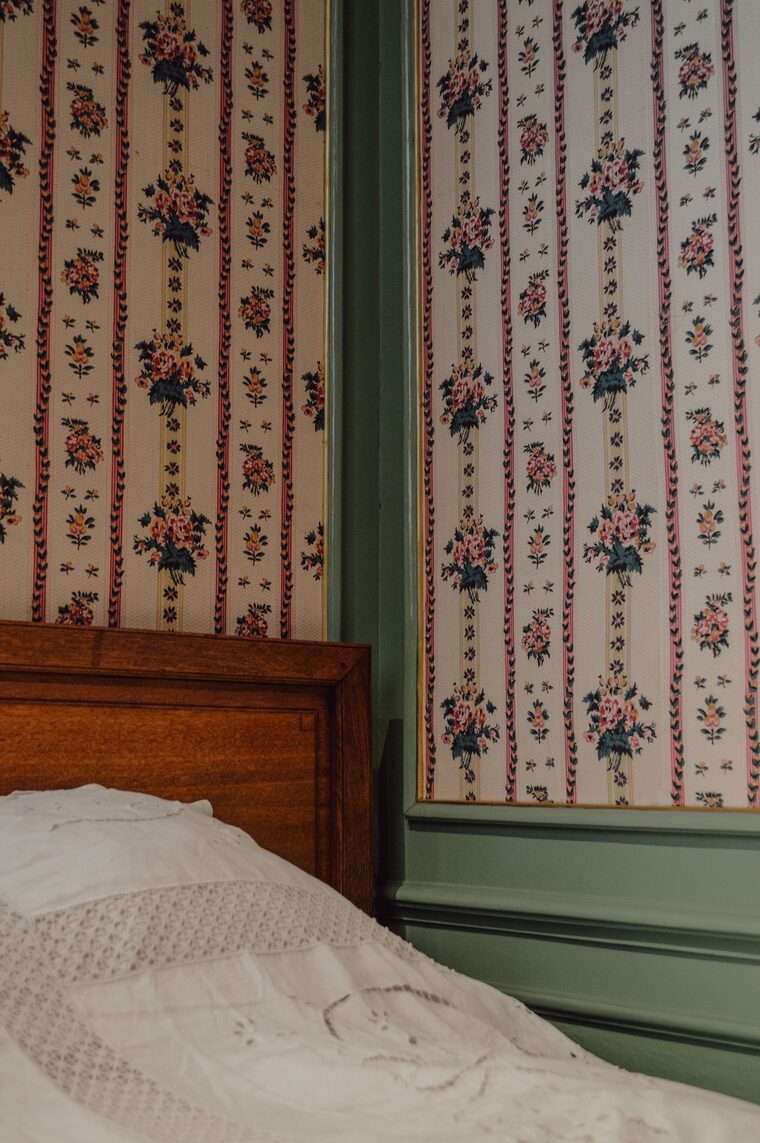 Vintage bedroom corner with striped floral wallpaper and a wooden bed frame