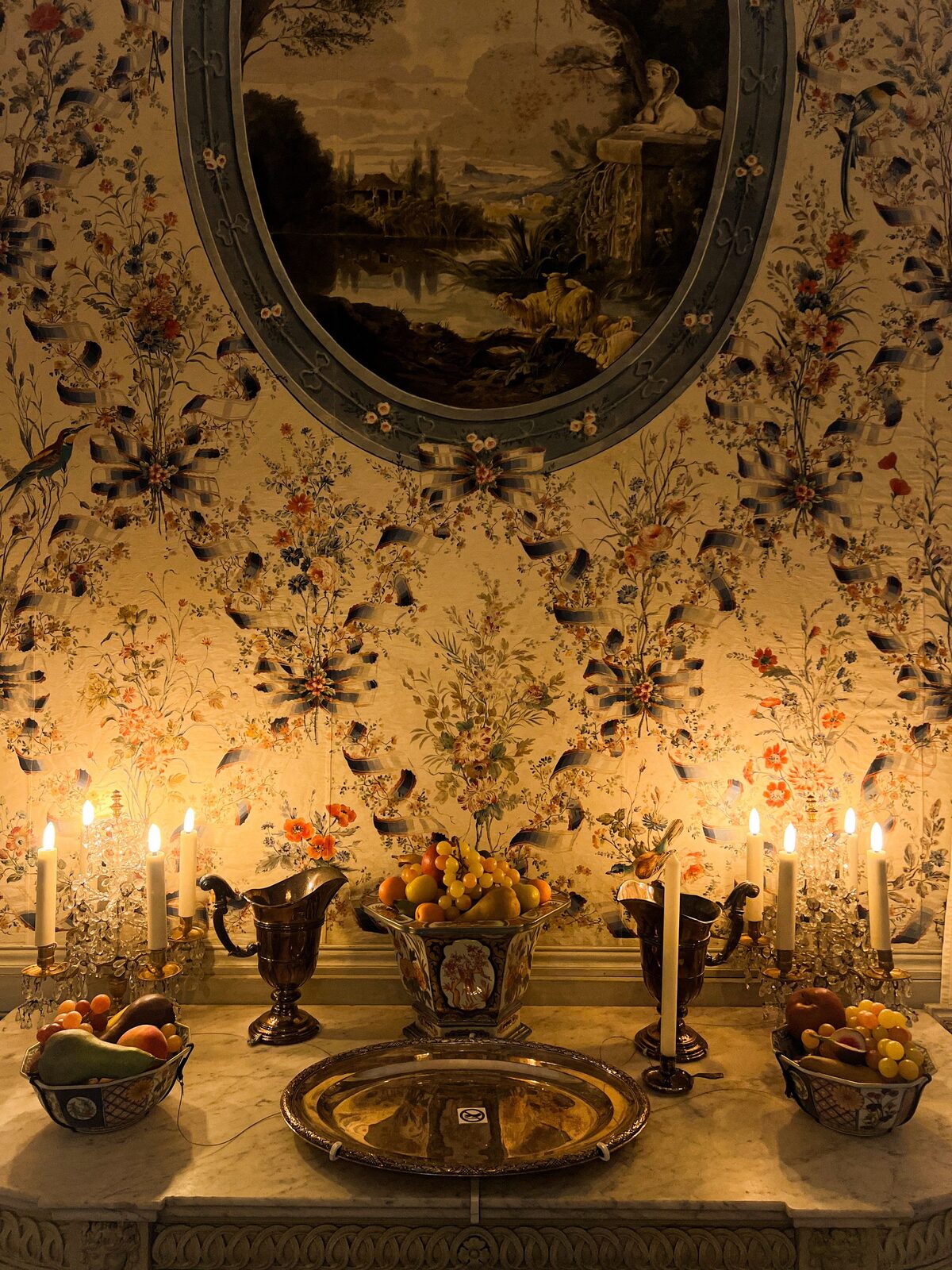 Candlelit dining room with a chinoiserie floral wallpaper feature wall and brass tableware